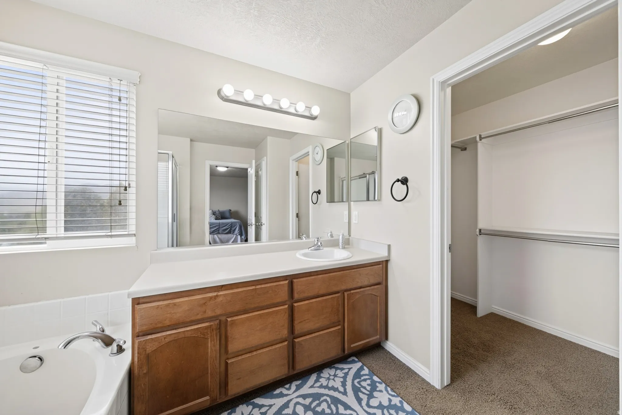 Built-in wood-finish vanity with a single basin sink and ample counter space, integrated soaking tub, and an open closet space with dual hanging rods