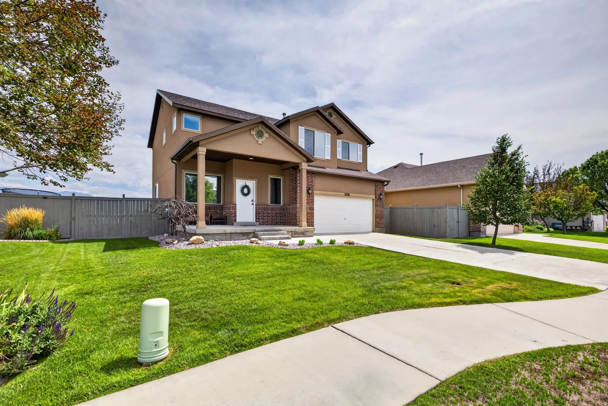 Stucco exterior with brick accents, covered front porch, attached two-car garage, concrete driveway, and established front landscaping