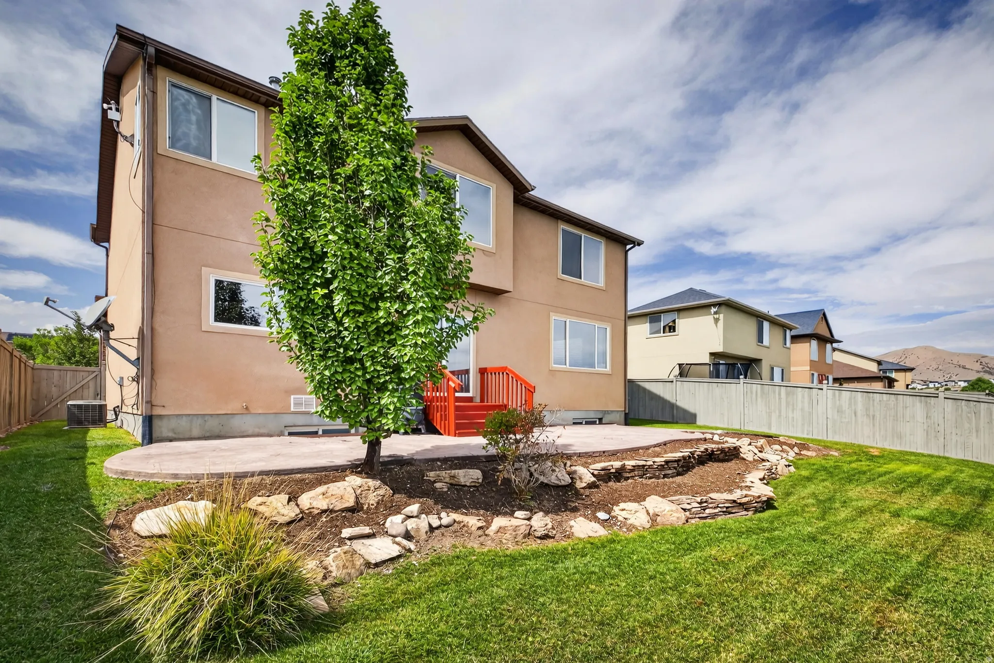 Expansive grass lawn, concrete patio, red wood-finish deck, and wood privacy fencing