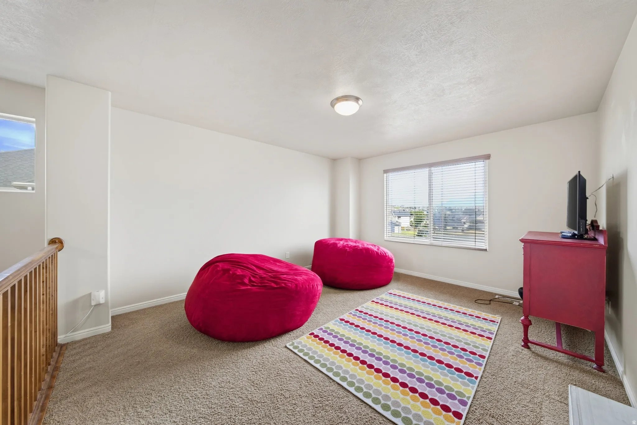 Carpeted bonus room with a window, ceiling-mounted light fixture, and wood railing