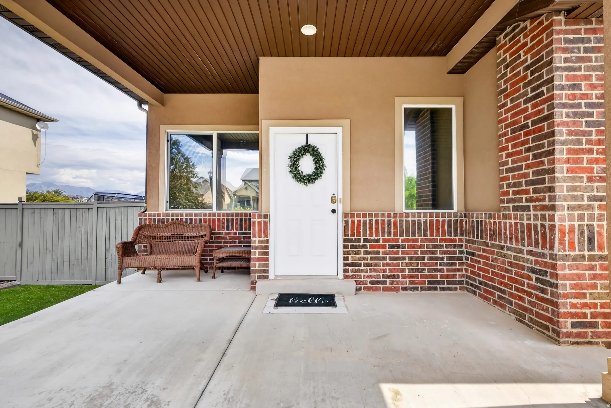 Inviting covered porch with a wood-finish ceiling, brick detailing, stucco siding, and a white entry door