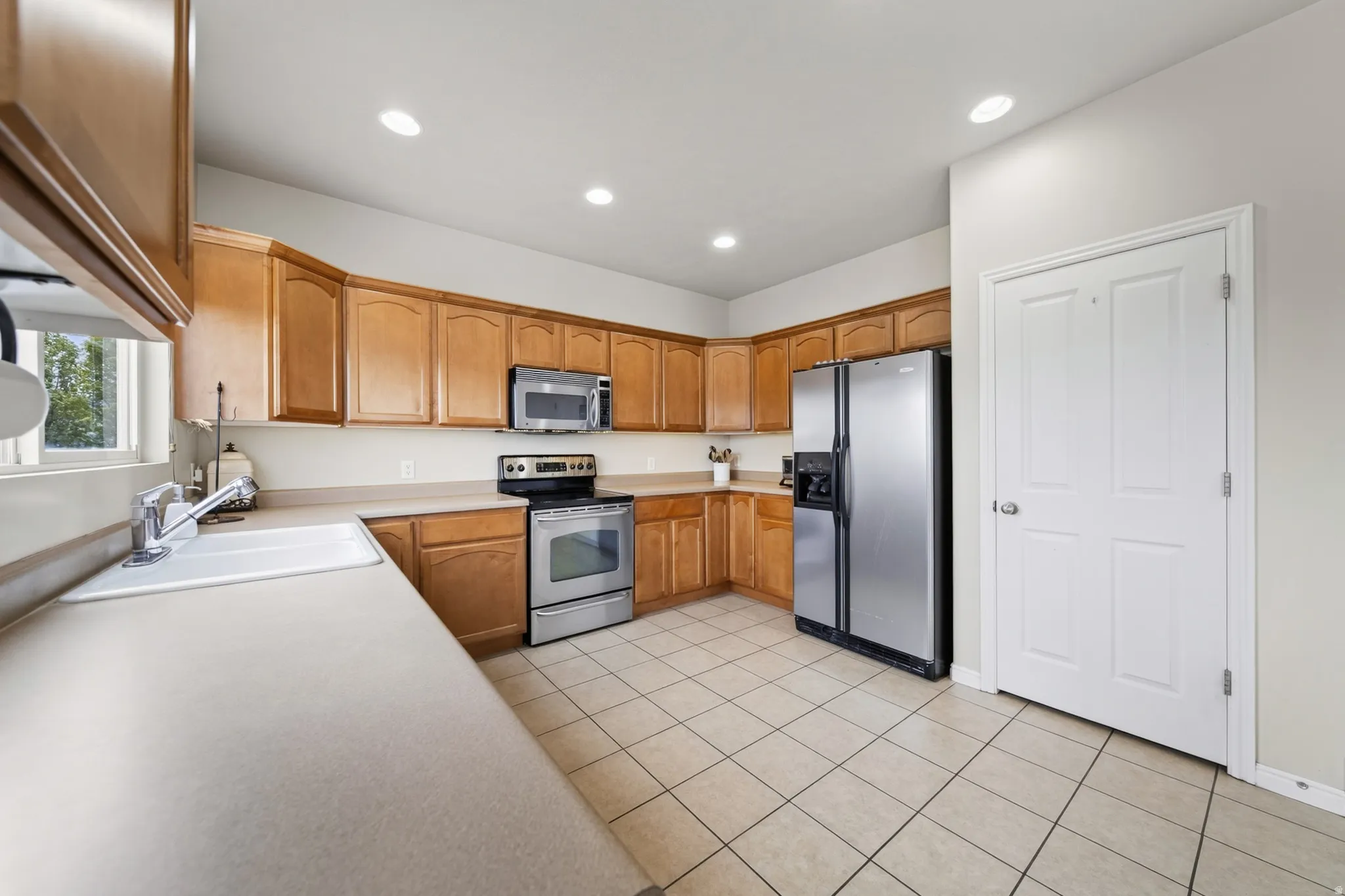 Wood-finish cabinetry, stainless steel appliances, recessed ceiling lighting, and ceramic tile flooring
