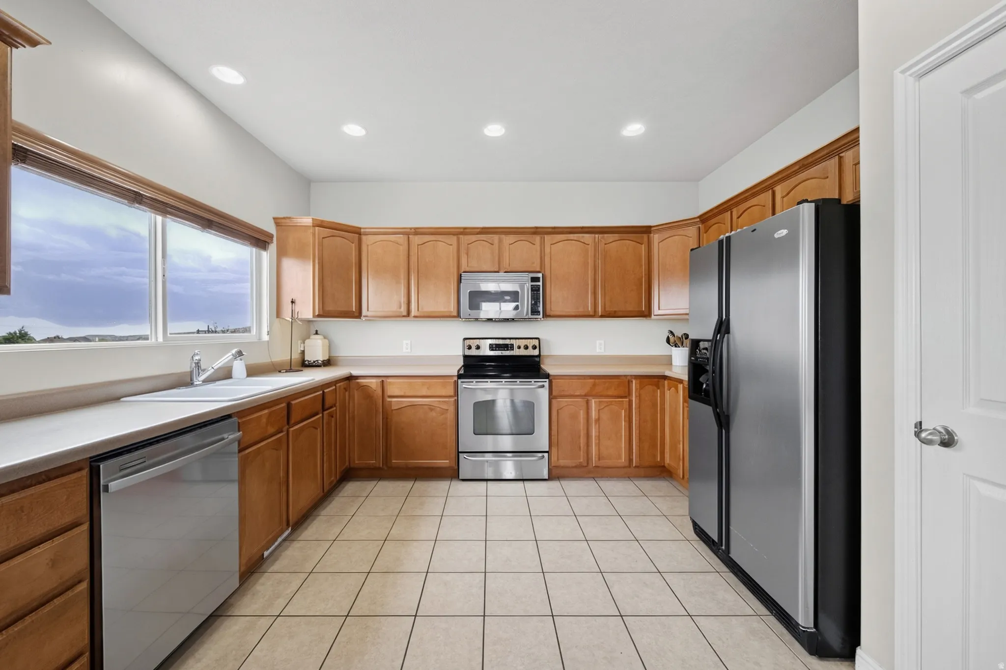 Kitchen featuring wood cabinetry, stainless steel appliances, a double basin sink, and tile flooring