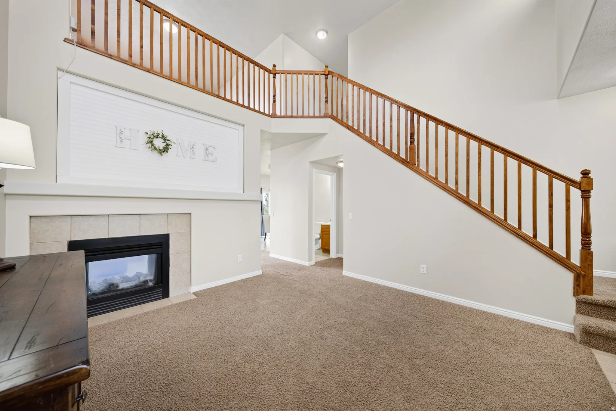 Vaulted ceiling featuring a gas fireplace with a tiled surround, a wood-finish staircase, and a carpeted floor