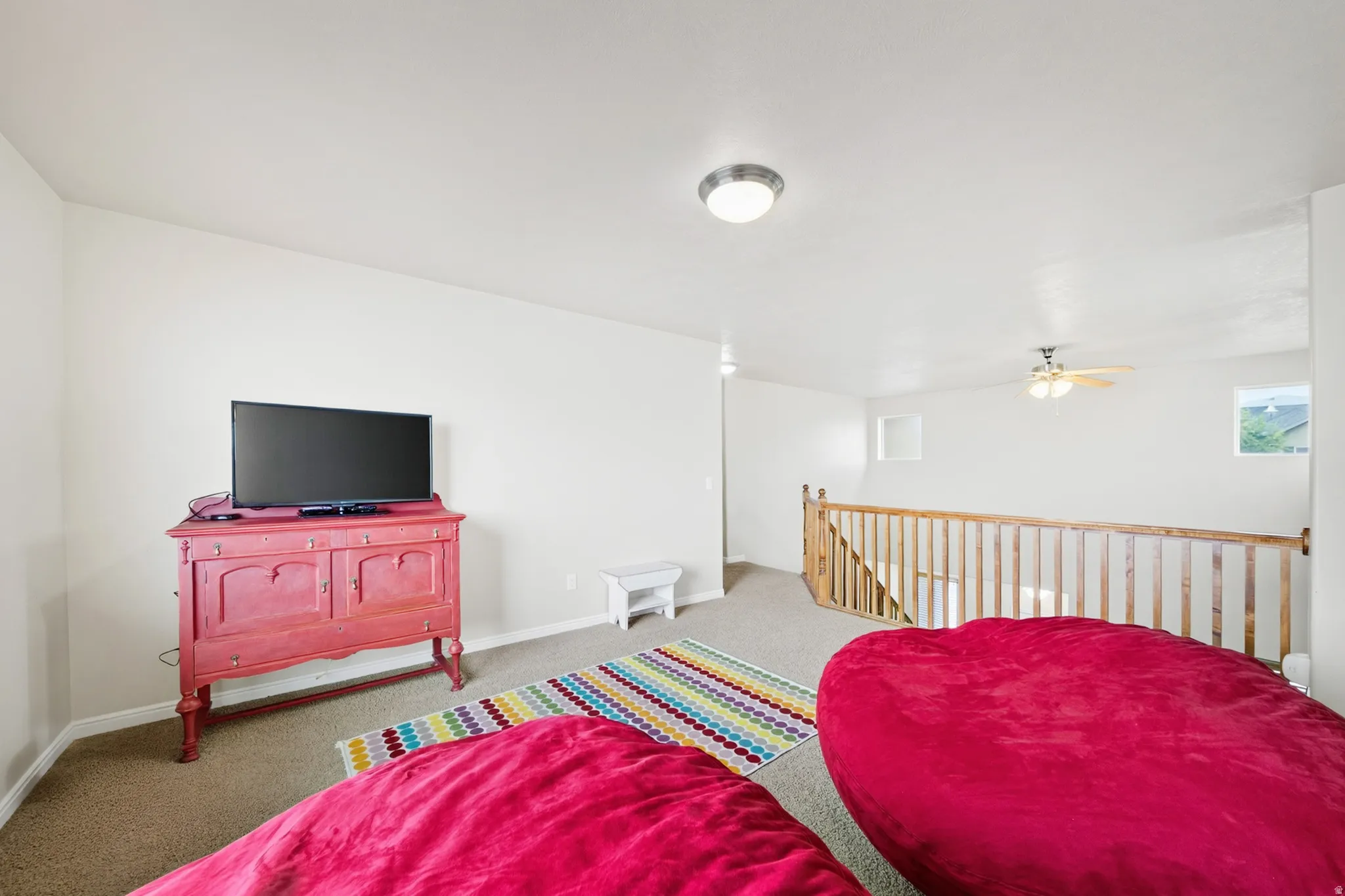 Carpeted open area featuring a wooden railing, flush mount ceiling light, and ceiling fan