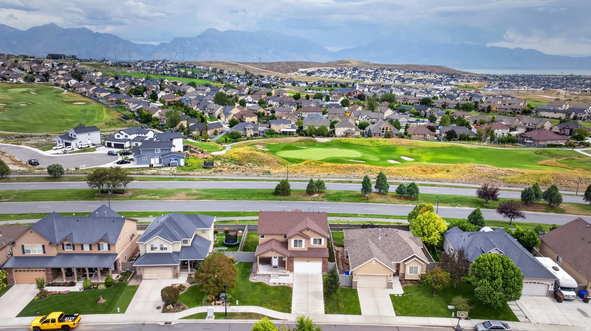 Suburban neighborhood with varied home styles, manicured lawns, and mature trees, featuring mountain backdrops and a golf course