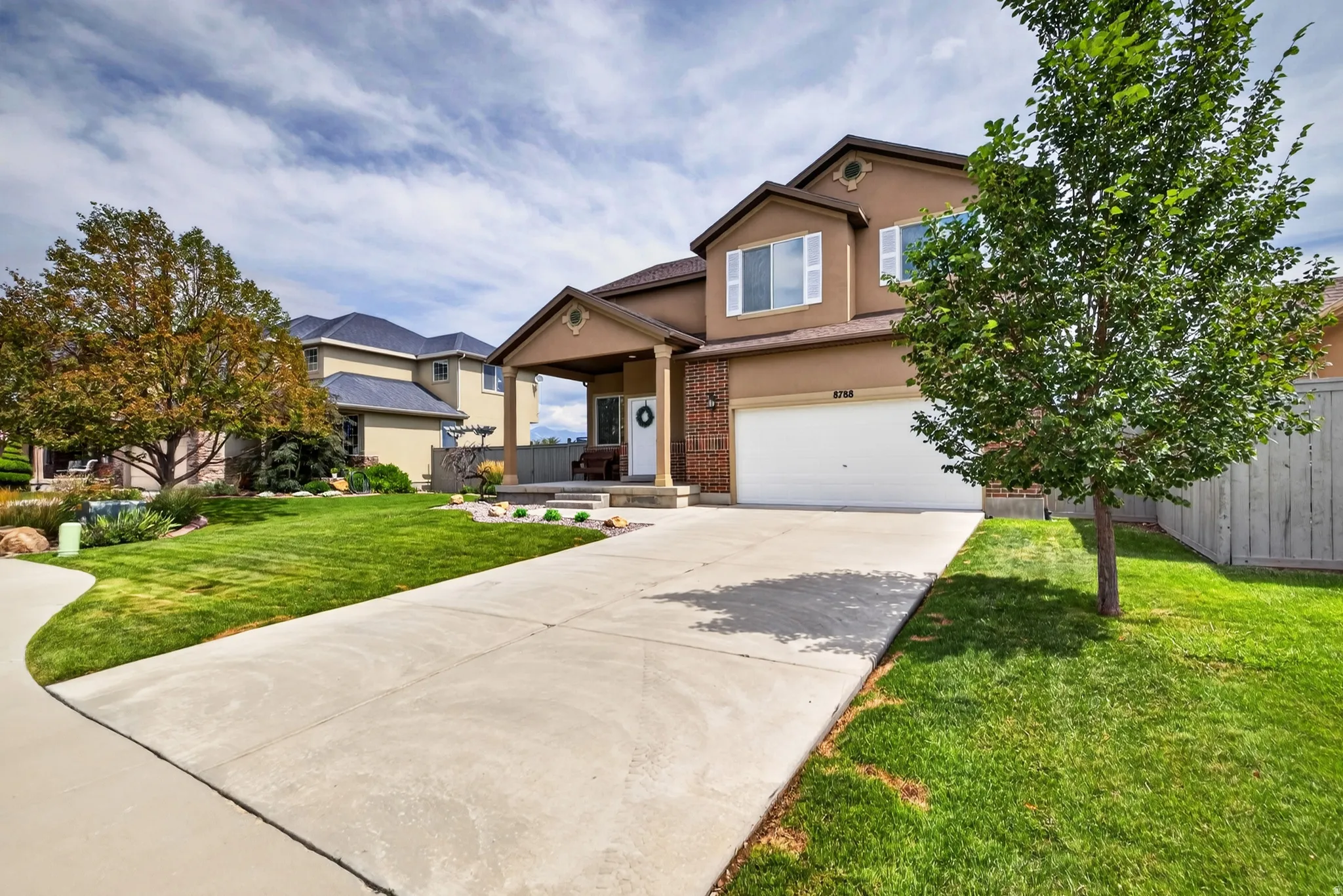 Two-story stucco and brick exterior, covered front porch, attached garage, concrete driveway, and manicured landscaping