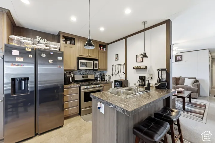 Kitchen featuring a stainless steel refrigerator, stainless steel range with microwave, wood-finish cabinetry, a peninsula with a double basin sink, and recessed lighting