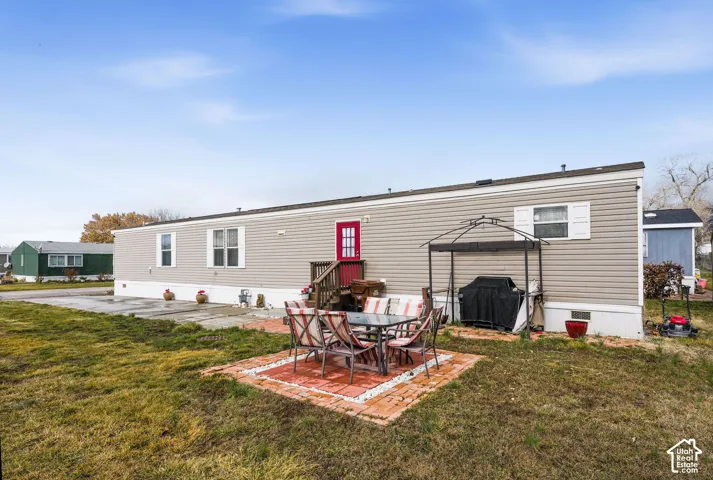 Grey siding exterior with white trim, red entry door, and a brick paver patio