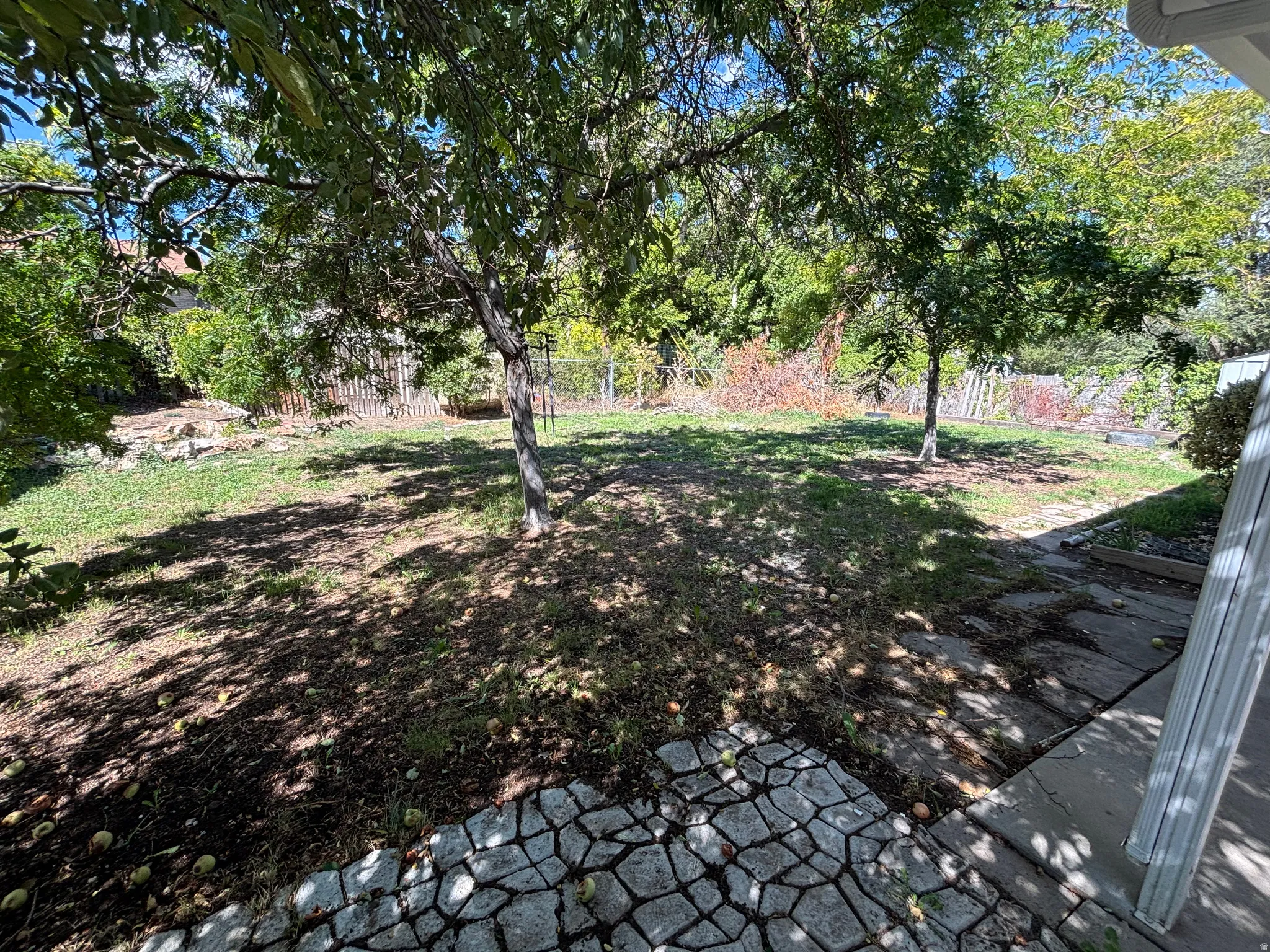 Expansive rear yard featuring mature trees, a partially sloped lawn, and a stone paver patio area