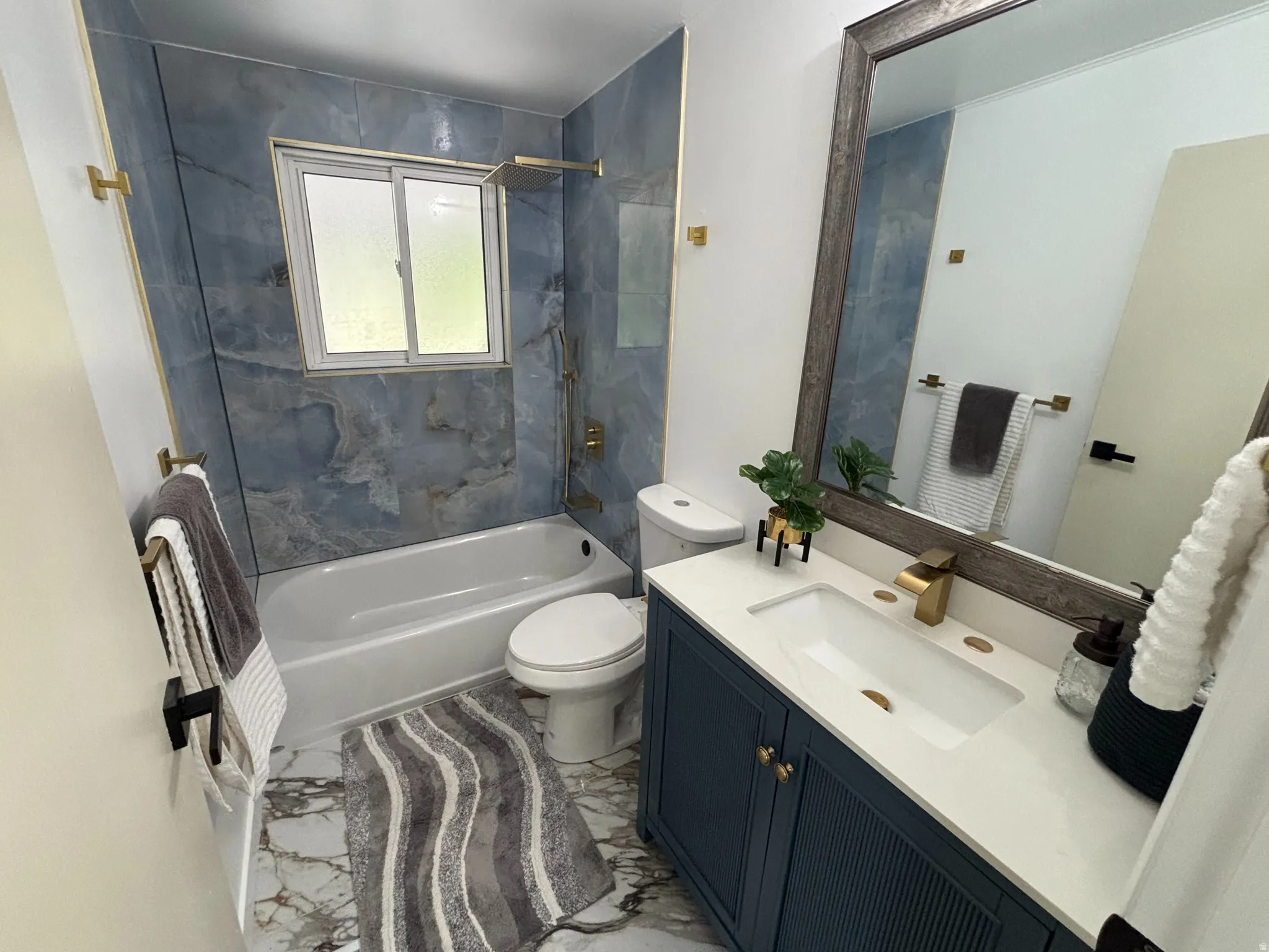 Bathroom featuring blue accent tiling, a white bathtub, a single vanity with a white countertop, gold-finish fixtures, and a framed mirror