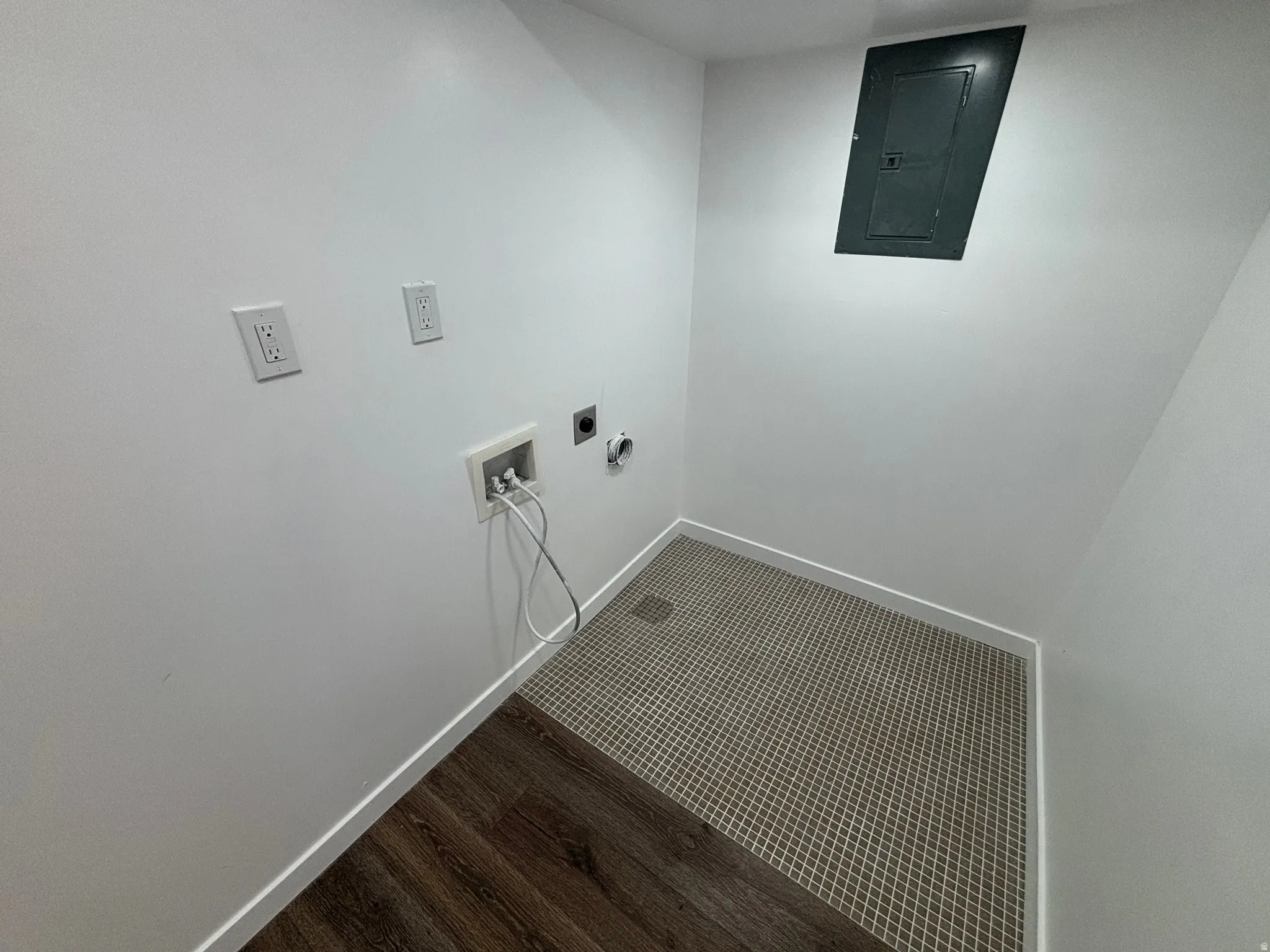 Utility area featuring white walls, a breaker box, and multi-surface flooring with wood-finish planks and patterned tile