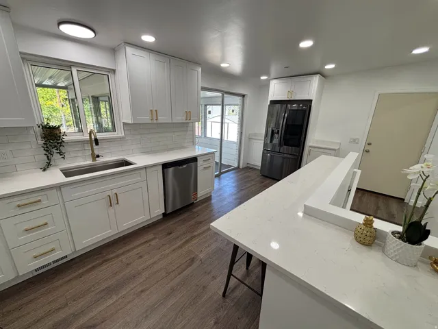 White shaker cabinetry with gold-finish hardware, stainless steel sink with gold-finish faucet, white subway tile backsplash, wood-finish flooring, and white countertops