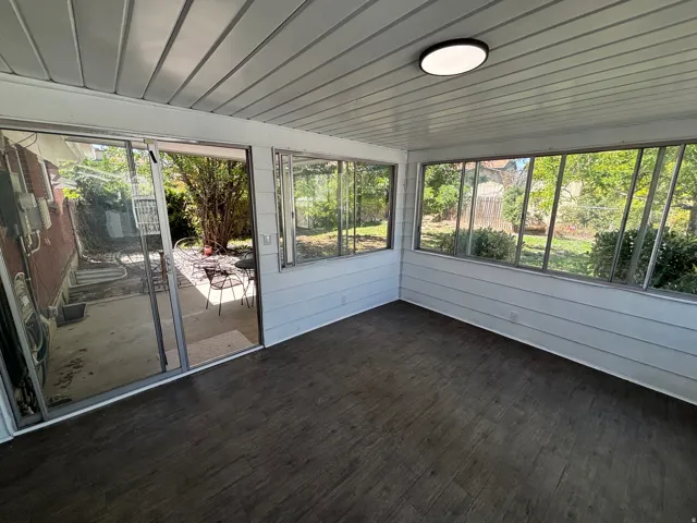 Enclosed patio featuring wood-finish flooring, white paneled walls, a ceiling-mounted light fixture, and large windows