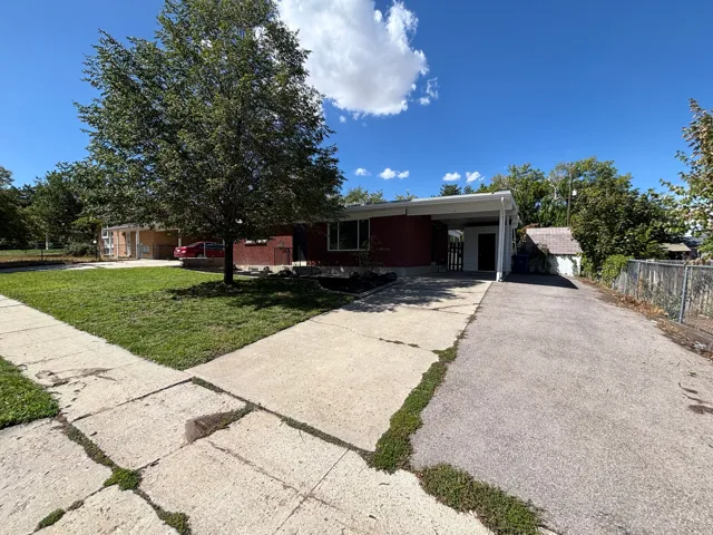 Red brick exterior featuring a white carport, concrete walkway, and a landscaped front yard with a mature tree