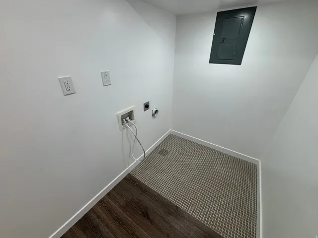 Utility area featuring white walls, a breaker box, and multi-surface flooring with wood-finish planks and patterned tile