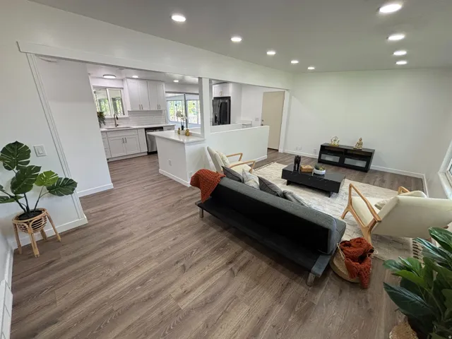 Open-concept living space featuring wood-finish flooring, recessed lighting, and a kitchen with white cabinetry and stainless steel appliances