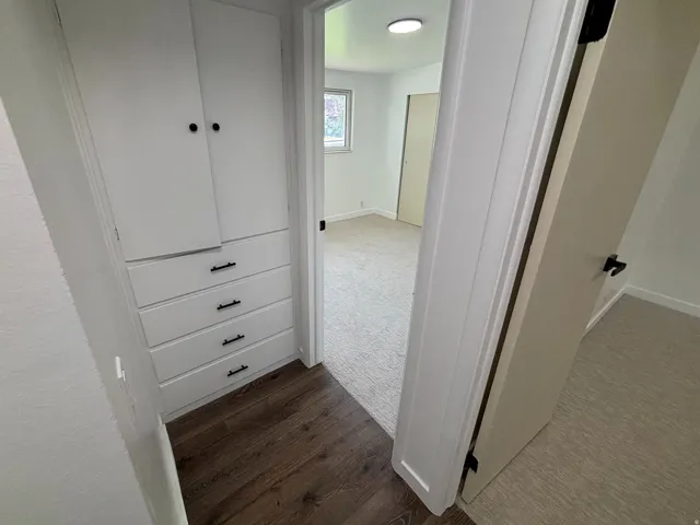 White built-in cabinetry with black hardware, wood-finish flooring, and light-colored carpeting