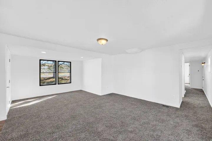Spacious room featuring neutral carpeting, a dual-pane window with black trim, and recessed lighting