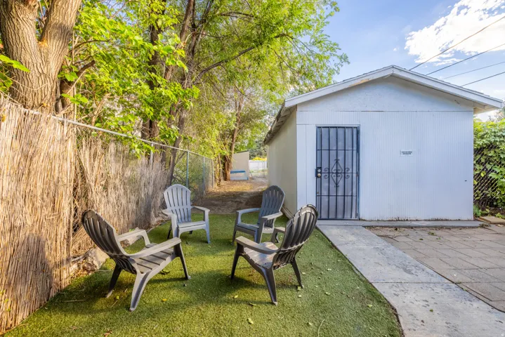 Detached outbuilding with a security door, adjacent to an artificial turf area, mature trees, and a privacy screen