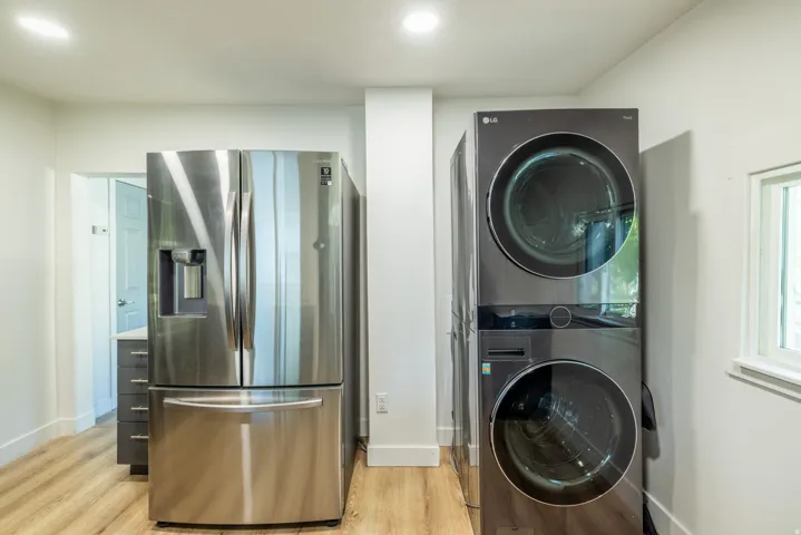 Stainless steel refrigerator with a water dispenser, stacked laundry appliances, recessed ceiling lighting, and wood-finish flooring