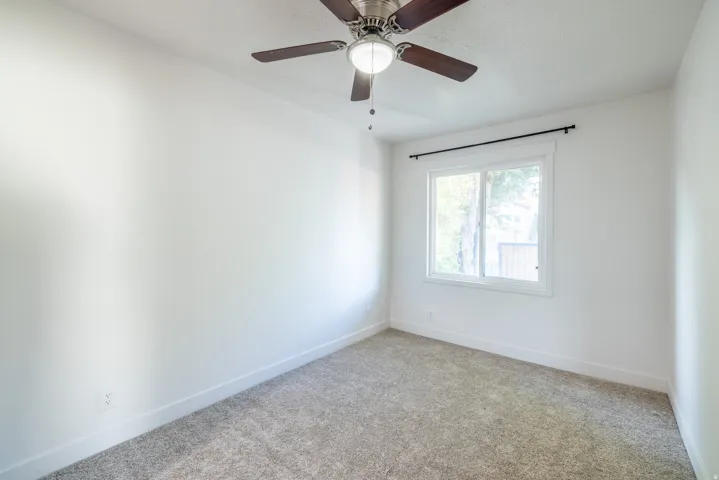 Light gray carpeting paired with white walls, a single window, and a ceiling fan with integrated lighting