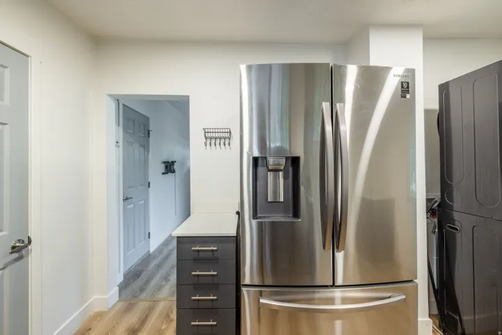 Stainless steel French door refrigerator, wood-finish flooring, white countertops, and dark cabinetry with silver hardware