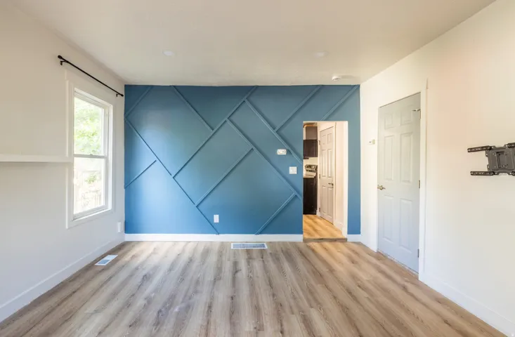 Bright, open bedroom showcasing pristine wood-finish flooring, fresh white walls, and a striking accent wall featuring geometric diamond paneling in soft blue