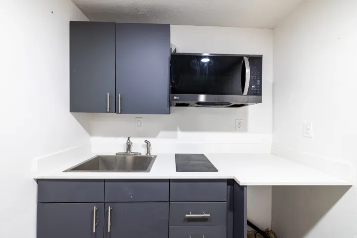 Kitchenette featuring a stainless steel sink, solid surface countertop, gray cabinetry, built-in microwave, and integrated cooktop