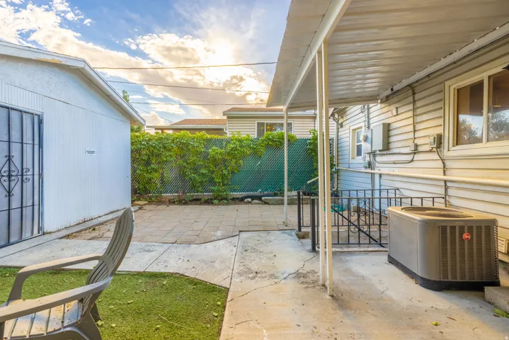 Covered patio area with concrete flooring, accented by a chain-link fence with lush greenery