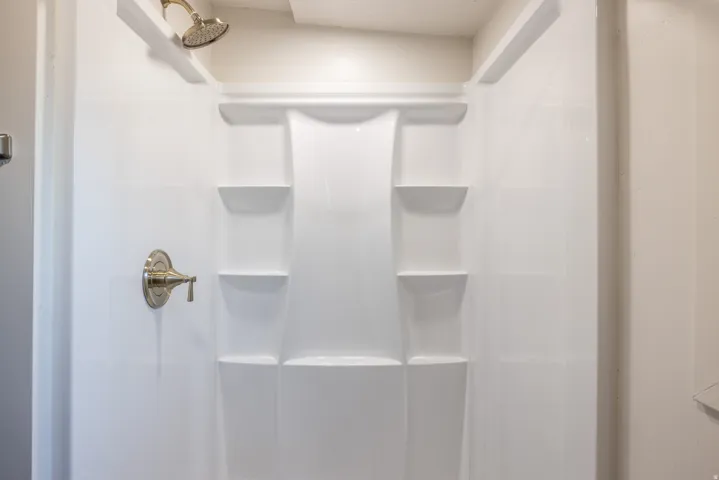 White shower surround with integrated shelving and a brushed nickel shower head
