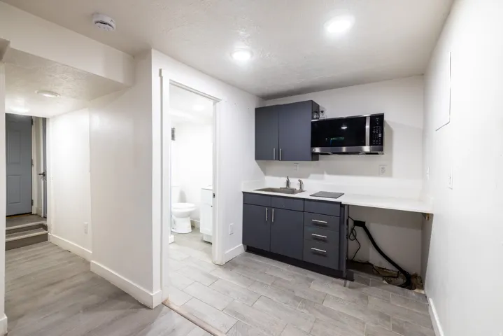 Compact kitchen area featuring dark gray cabinetry, stainless steel sink, built-in microwave, and solid surface countertops
