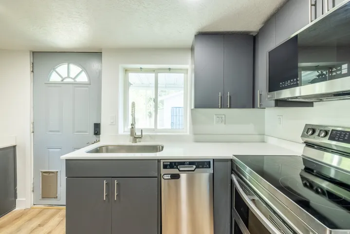 Modern kitchen featuring gray cabinetry, stainless steel appliances, a white solid surface countertop, and wood-finish flooring