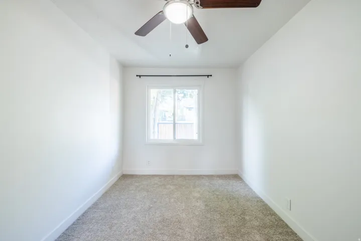 Neutral color palette, window with black hardware, ceiling fan, carpet flooring, and white trim