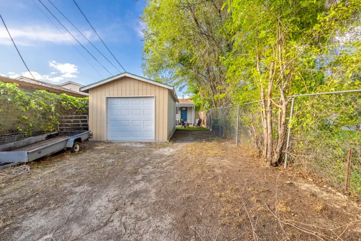 Detached garage with a paneled door, chain-link fencing, and mature trees
