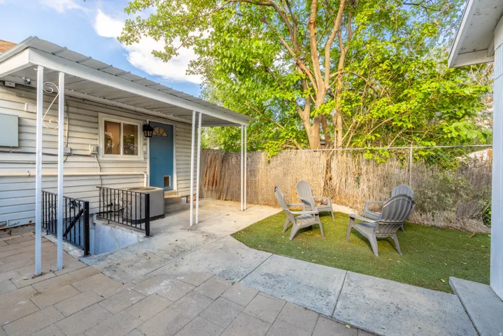 Covered patio area with concrete and paver flooring, artificial turf, and a wood-slat fence