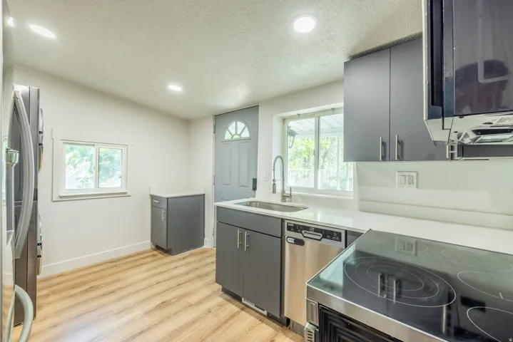 Modern kitchen featuring wood-finish flooring, dark gray cabinetry, stainless steel appliances, a kitchen sink with a gooseneck faucet, and white countertops