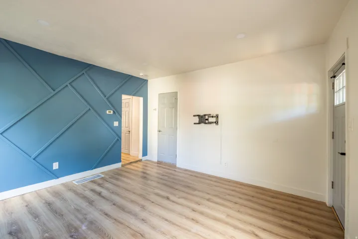 Accent wall featuring geometric paneling, wood-finish flooring, white trim, and a white entry door with frosted glass panels