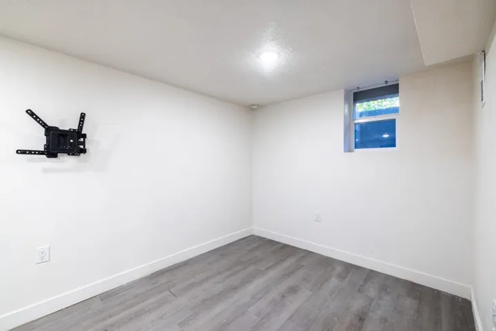 Recessed lighting, wood-finish flooring, white walls, and a window with a roller shade