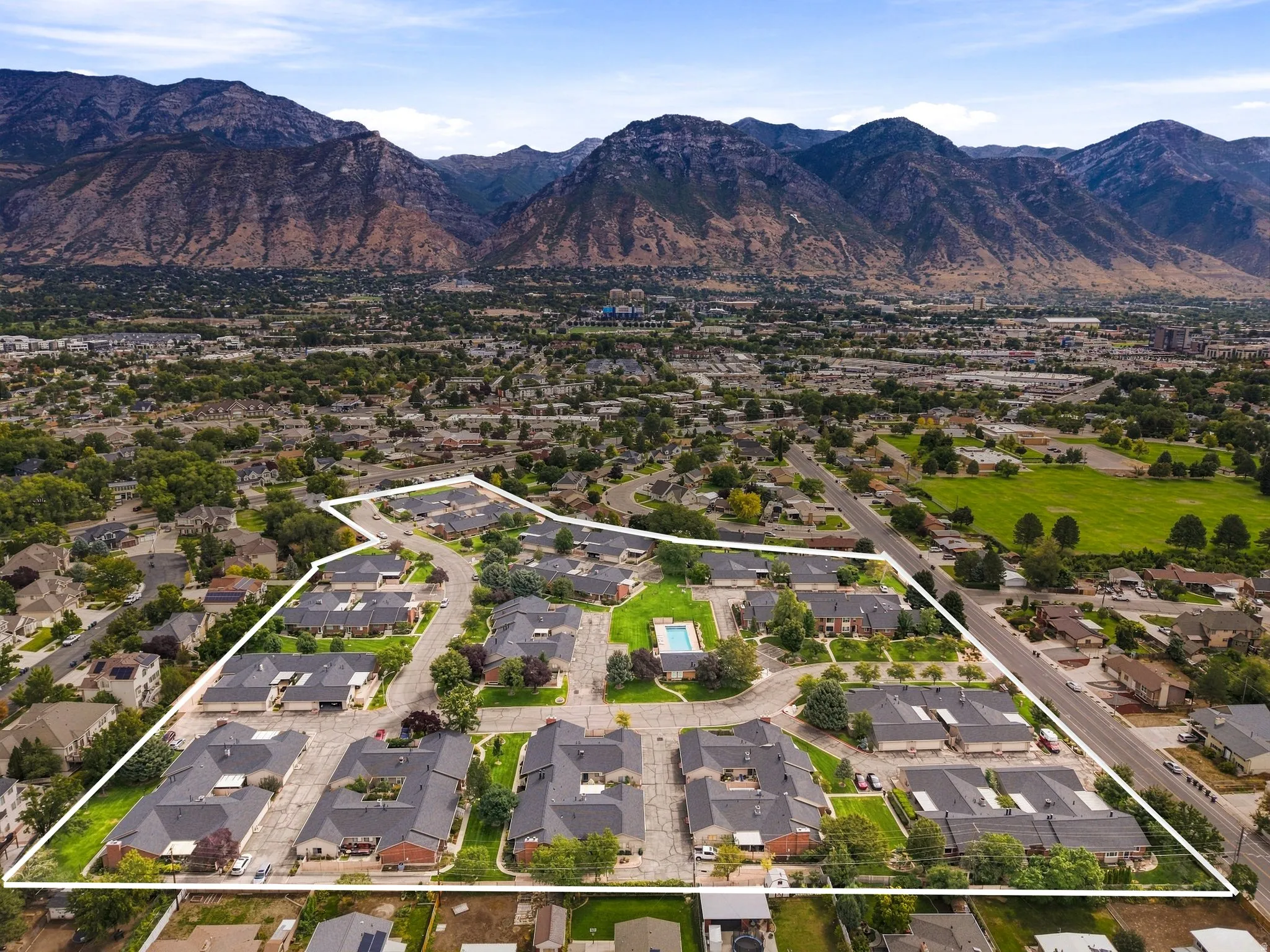 Mountain backdrop, residential development with multiple buildings, paved roads, central community pool, and surrounding green spaces