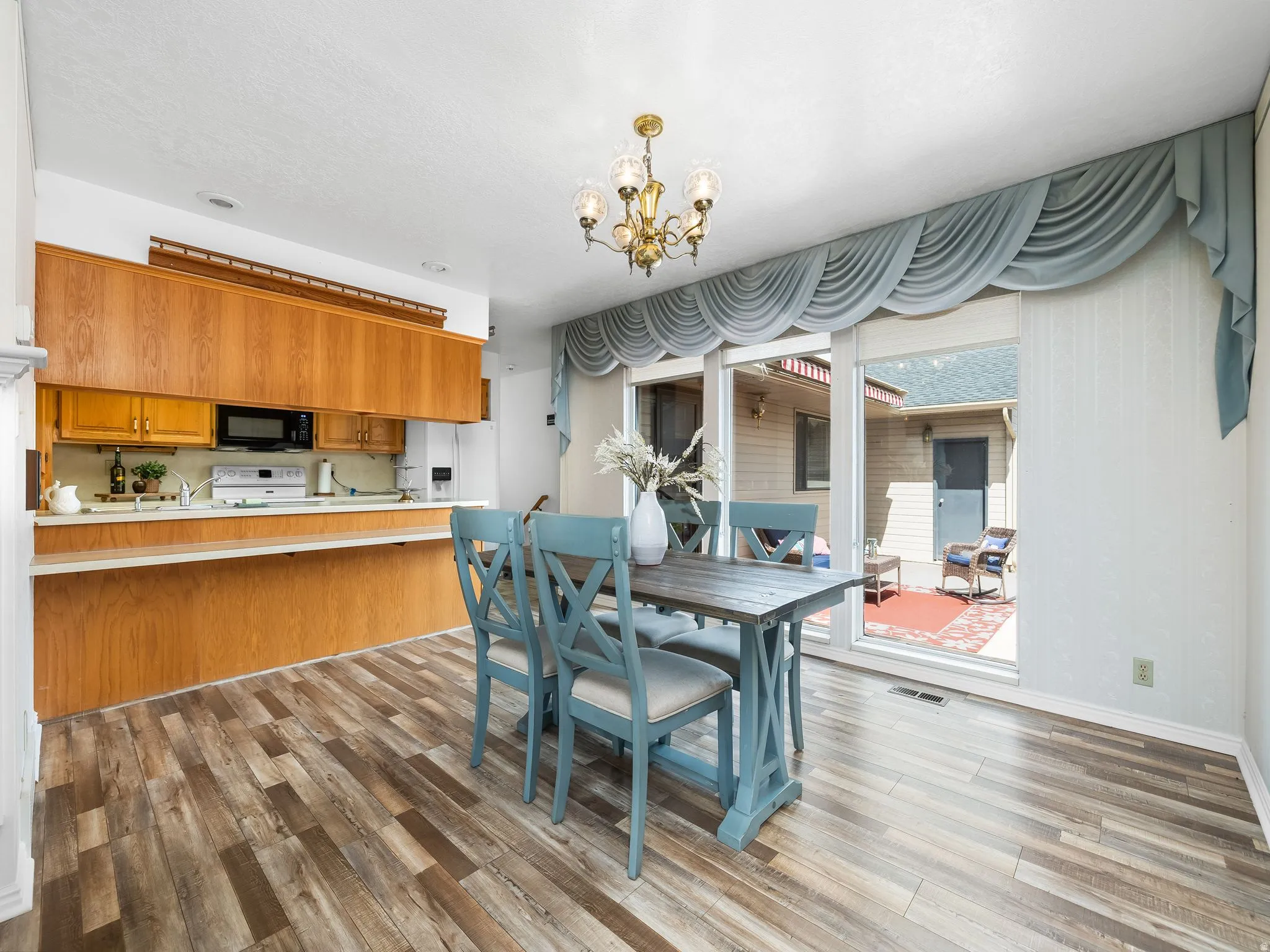 Hardwood-finish flooring, brass chandelier, wood cabinetry, built-in microwave, and sliding glass door