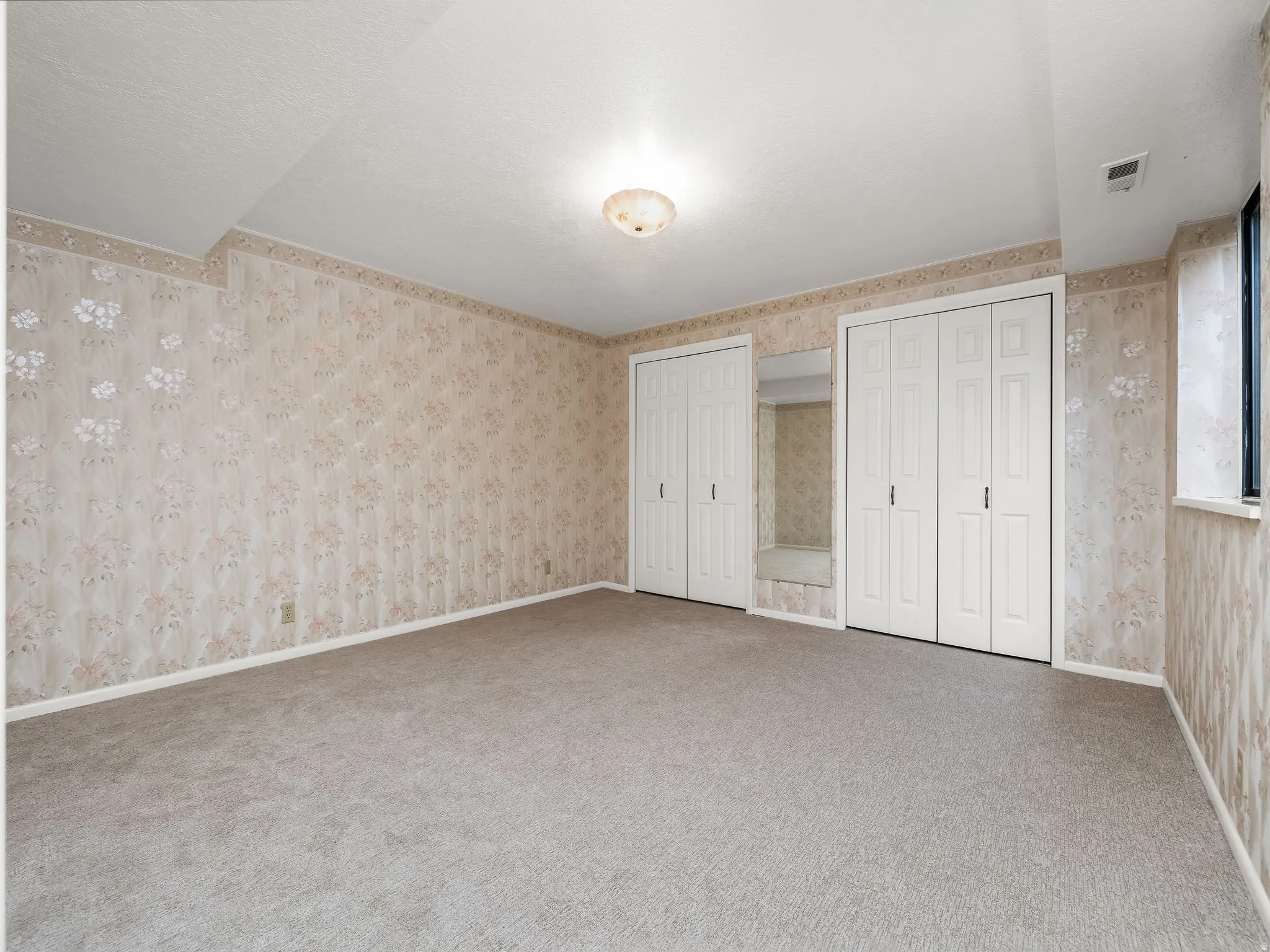 Carpeted room featuring floral wallpaper, white bi-fold closet doors, and built-in mirror
