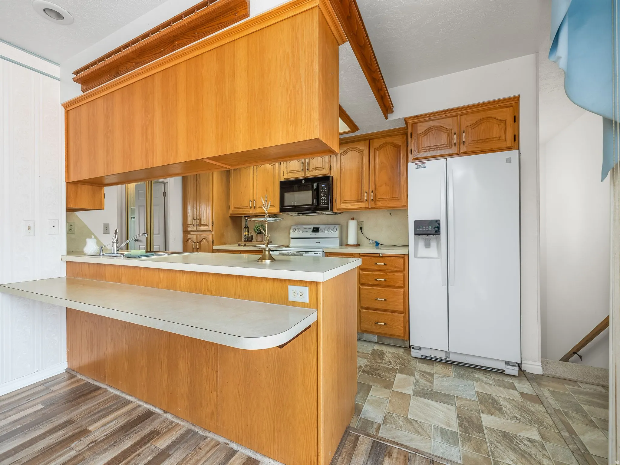Kitchen featuring wood-finish cabinetry, built-in microwave, white side-by-side refrigerator, and a breakfast bar