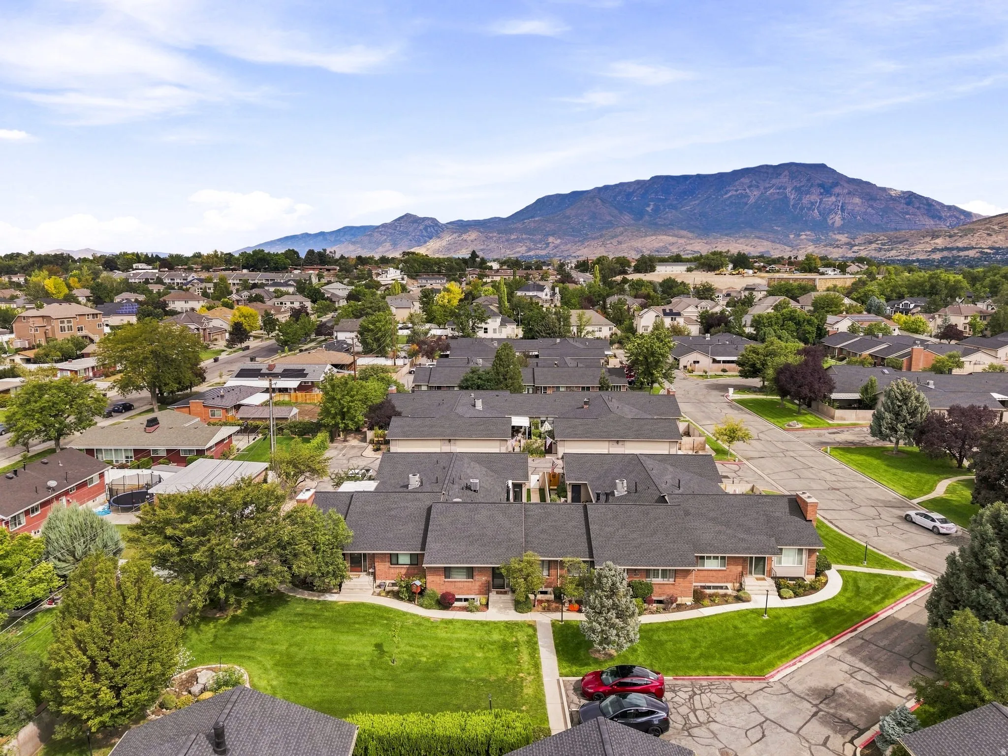 Expansive suburban neighborhood with mountain scenery, featuring a collection of brick properties with dark shingle roofs, and mature landscaping