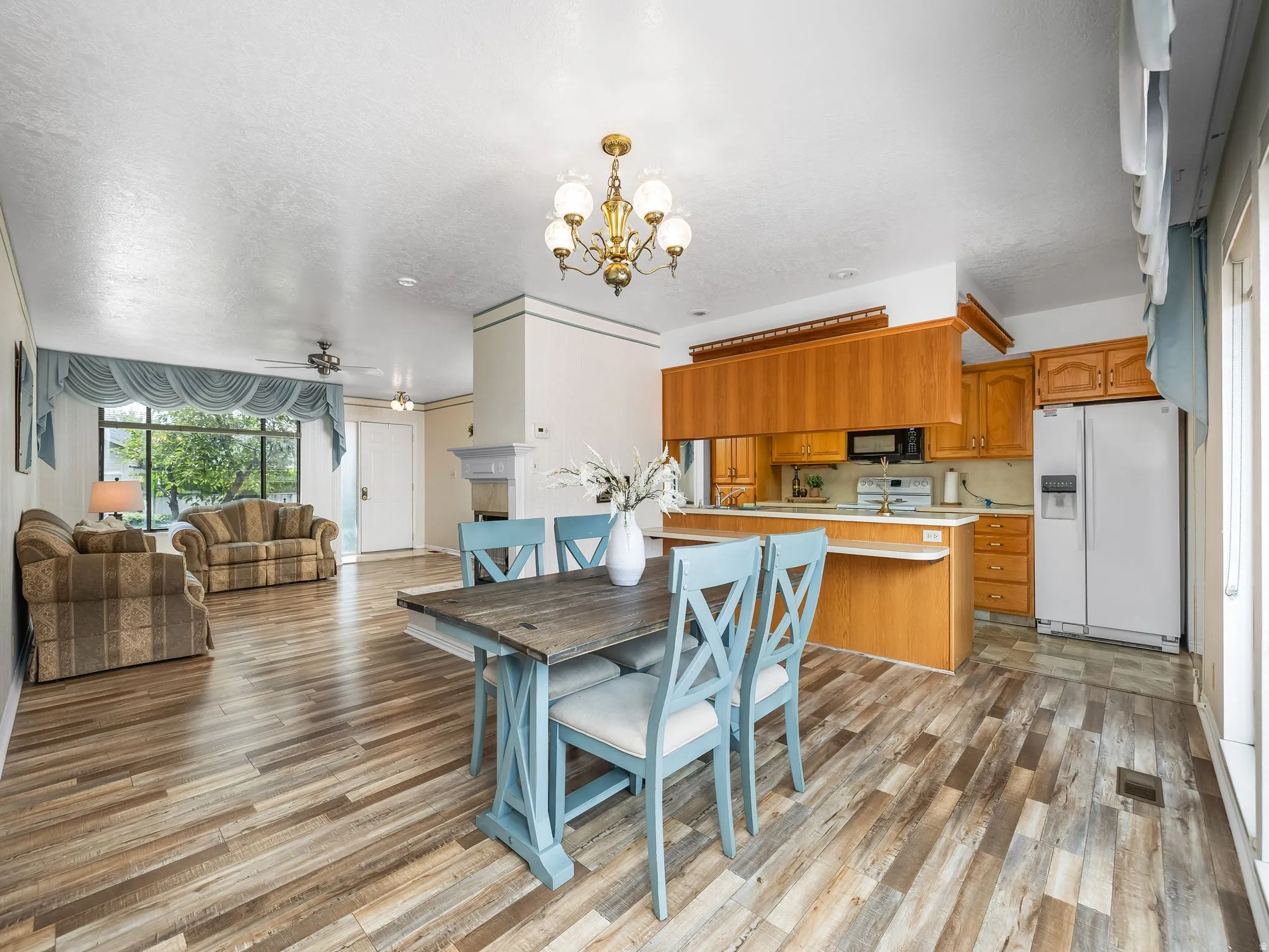 Open-concept layout with wood-finish flooring, a kitchen featuring wood cabinetry, white appliances, and a breakfast bar, and a living area with a large picture window