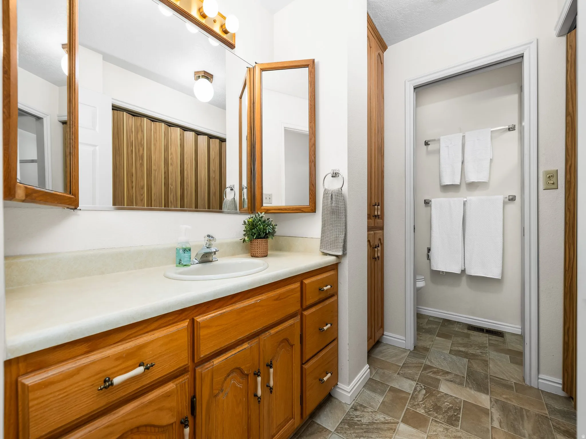 Bathroom vanity with wood-finish cabinetry, a drop-in sink, and a light-toned countertop