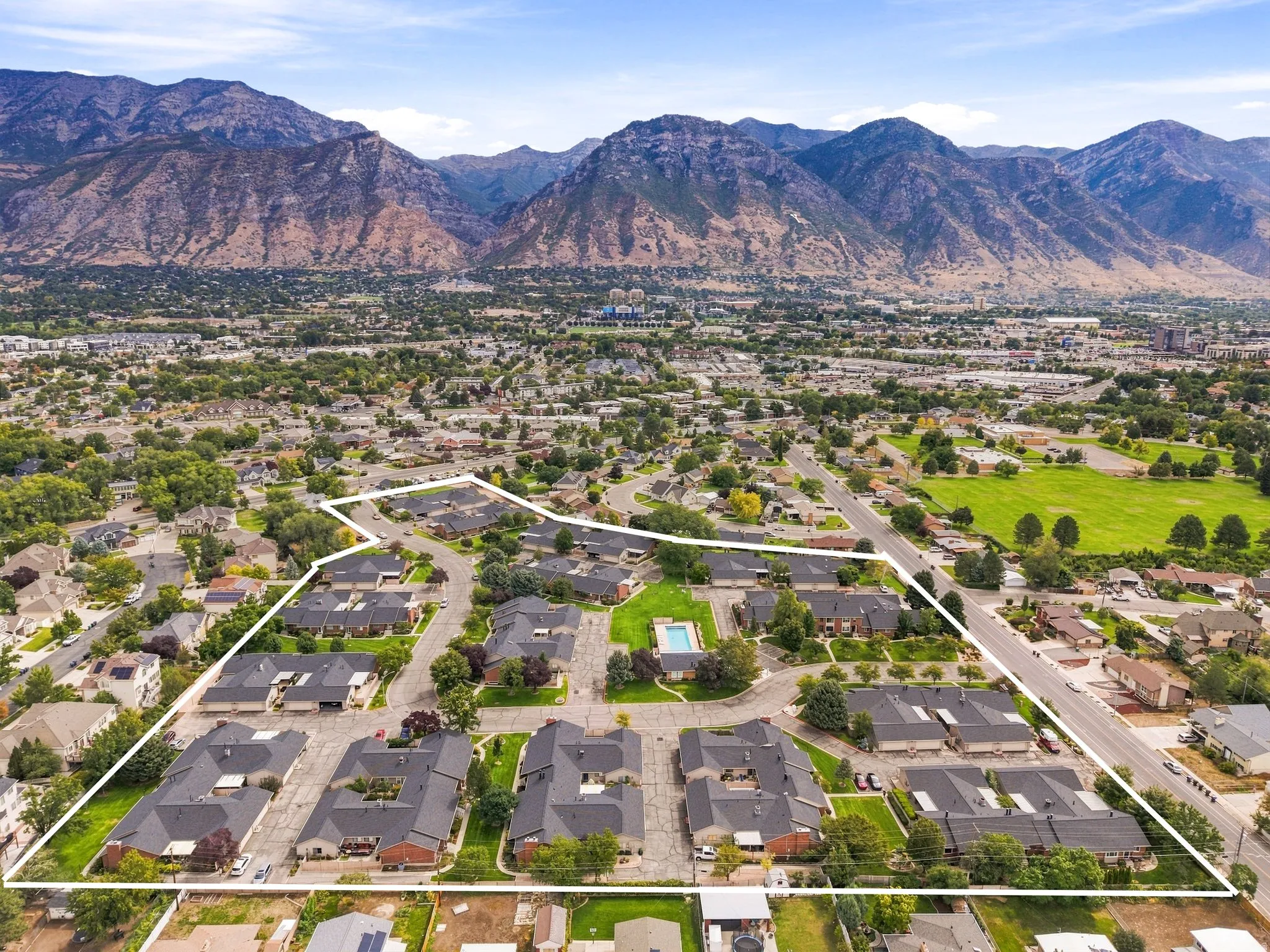 Residential development featuring multiple buildings, paved roads, a central swimming pool, and surrounding green spaces