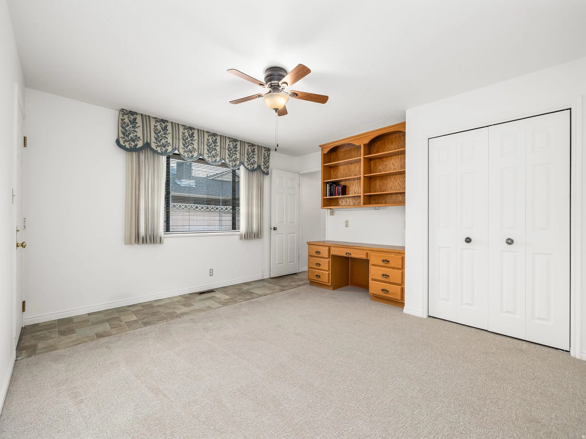 Built-in desk with shelving, ceiling fan, and bi-fold closet doors