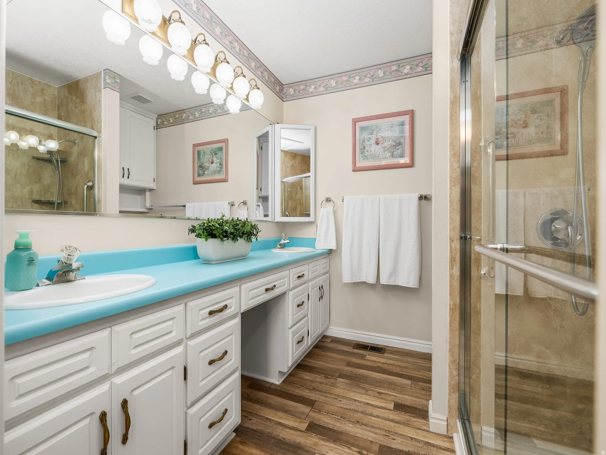 Double vanity with integrated sinks, white cabinetry, wood-finish flooring, and a glass-enclosed shower
