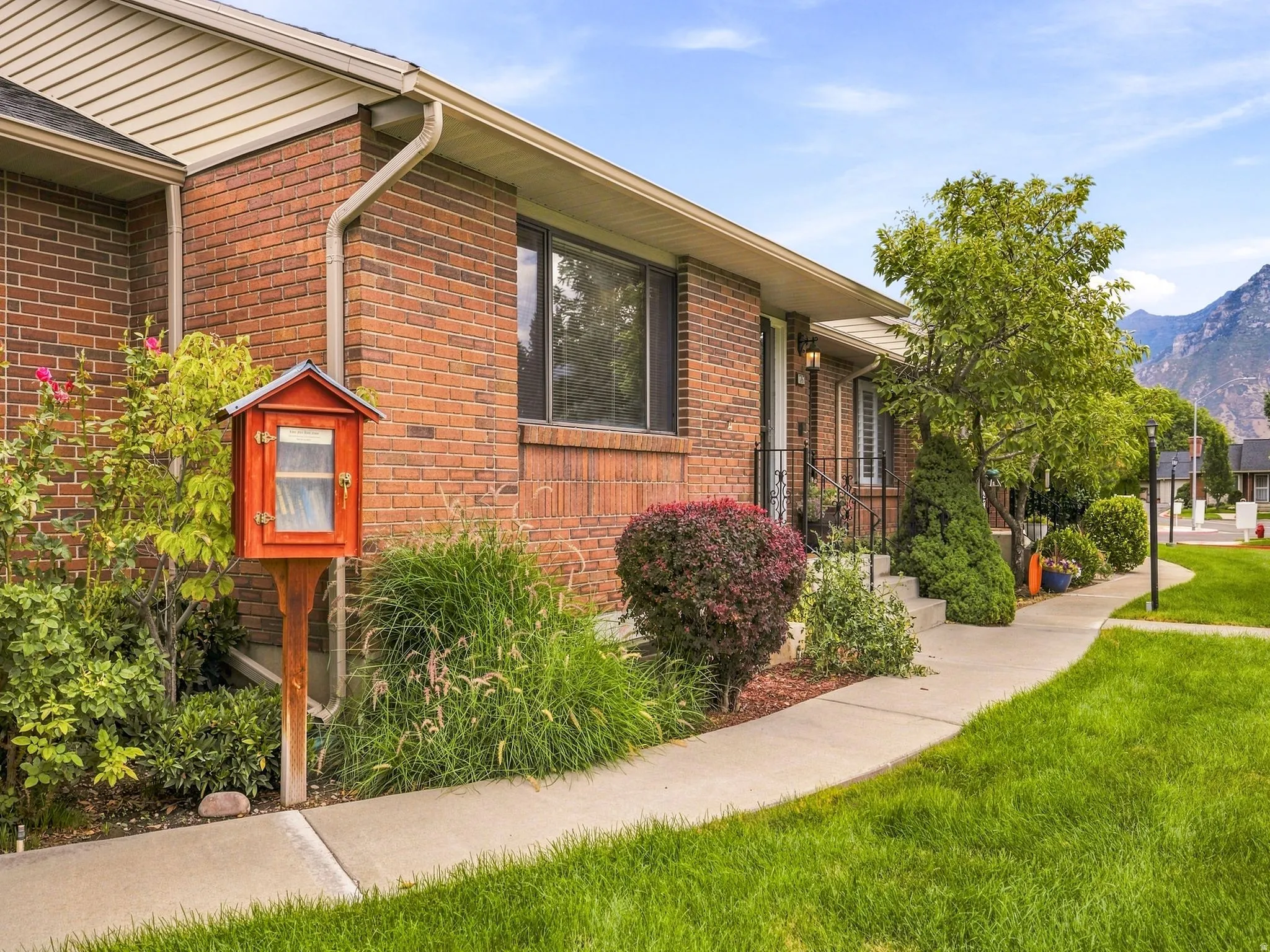 Brick exterior with white soffit, mature landscaping, concrete pathway, and mountain backdrop